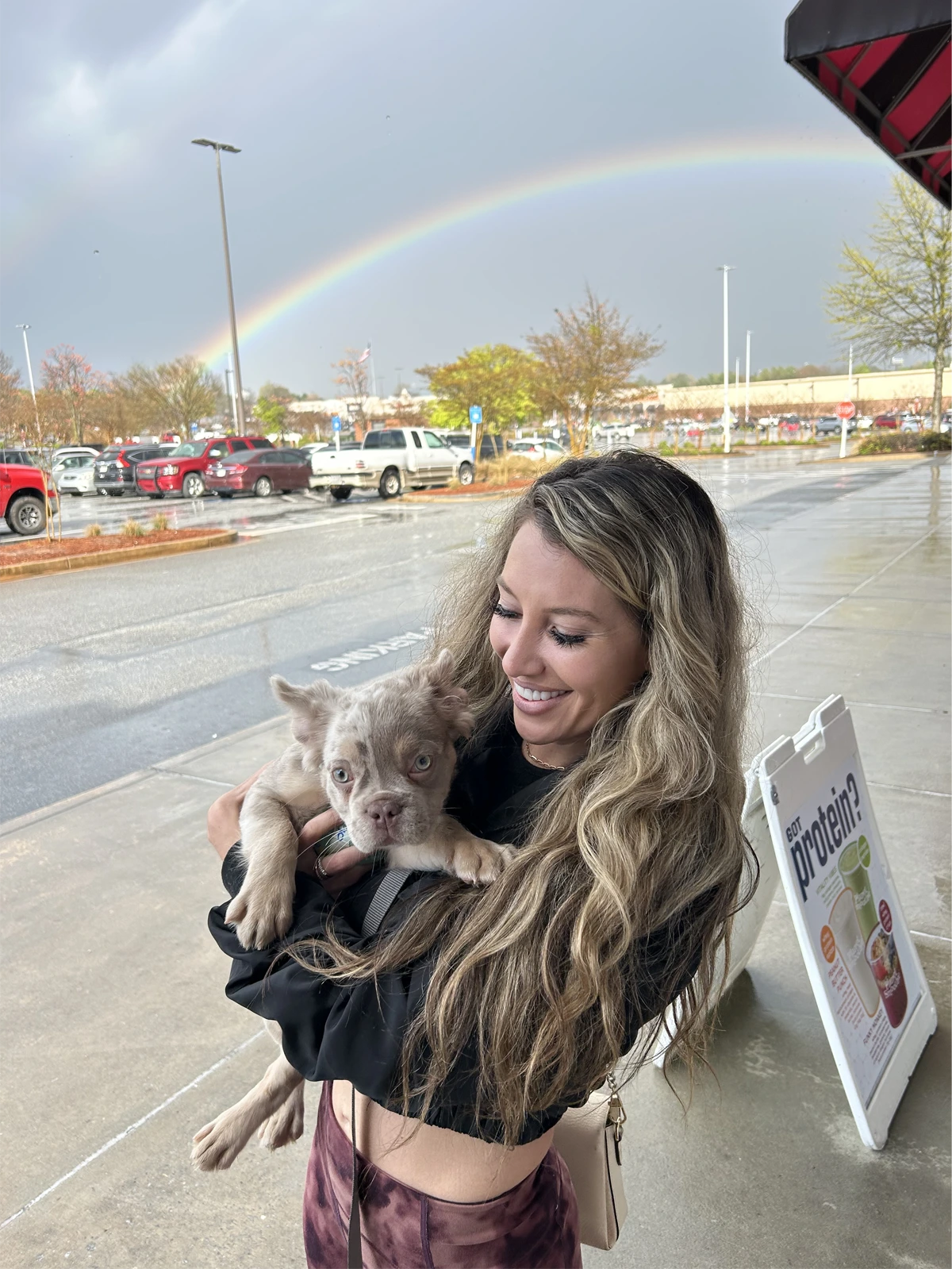 Woman holding Frenchie puppy outdoors with rainbow